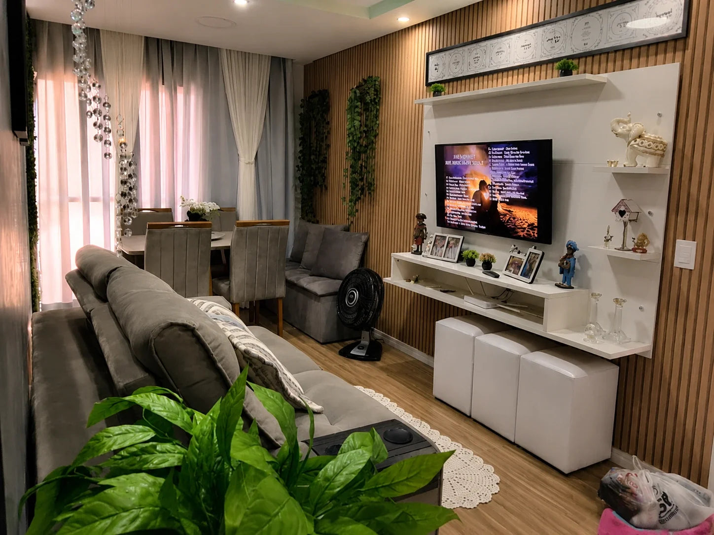 Panel de TV blanco con estantes flotantes en un living pequeño cálido, con sillón gris y pared revestida en madera